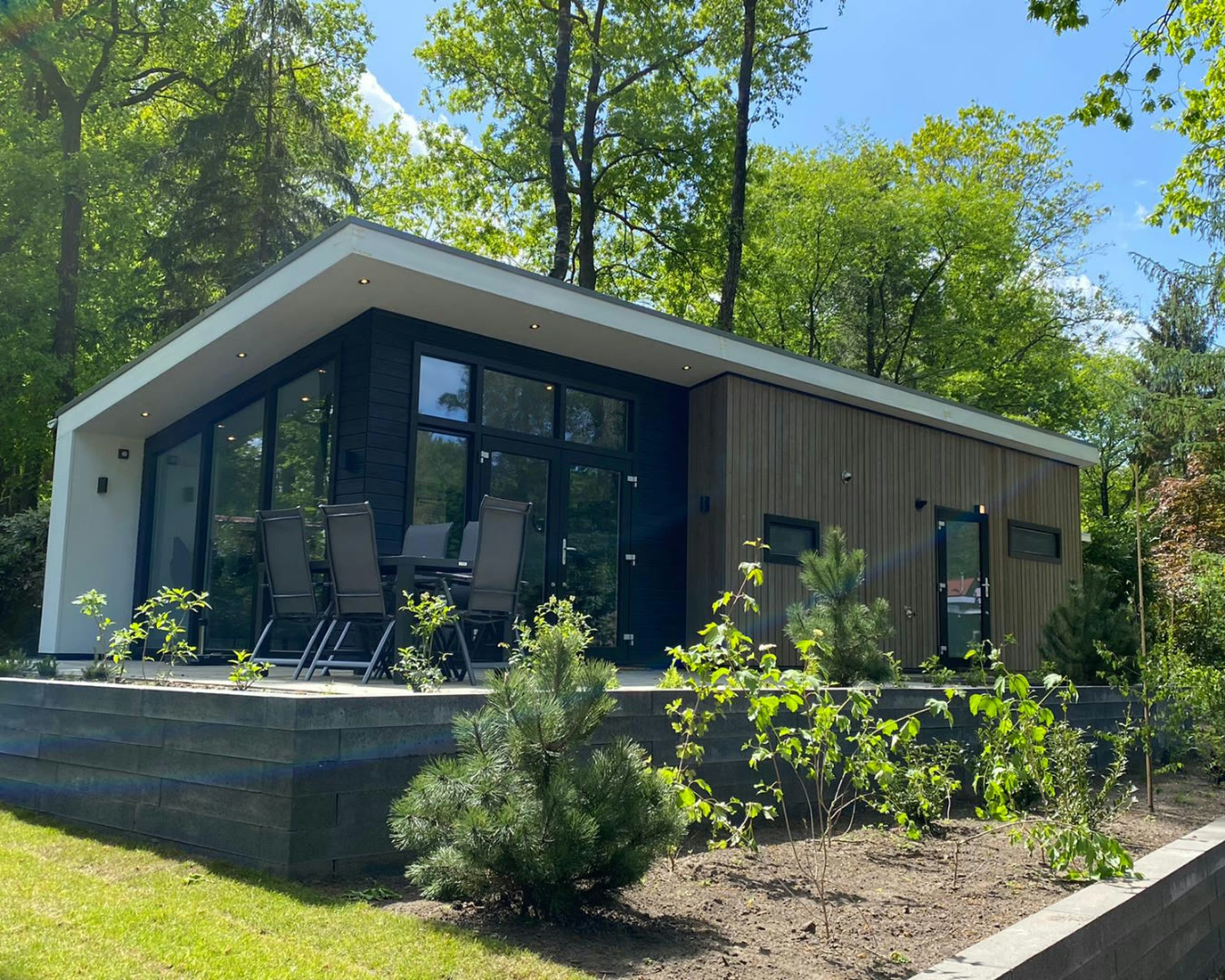 Moderne donkere mantelzorgwoning met grote ramen in een bosrijke tuin