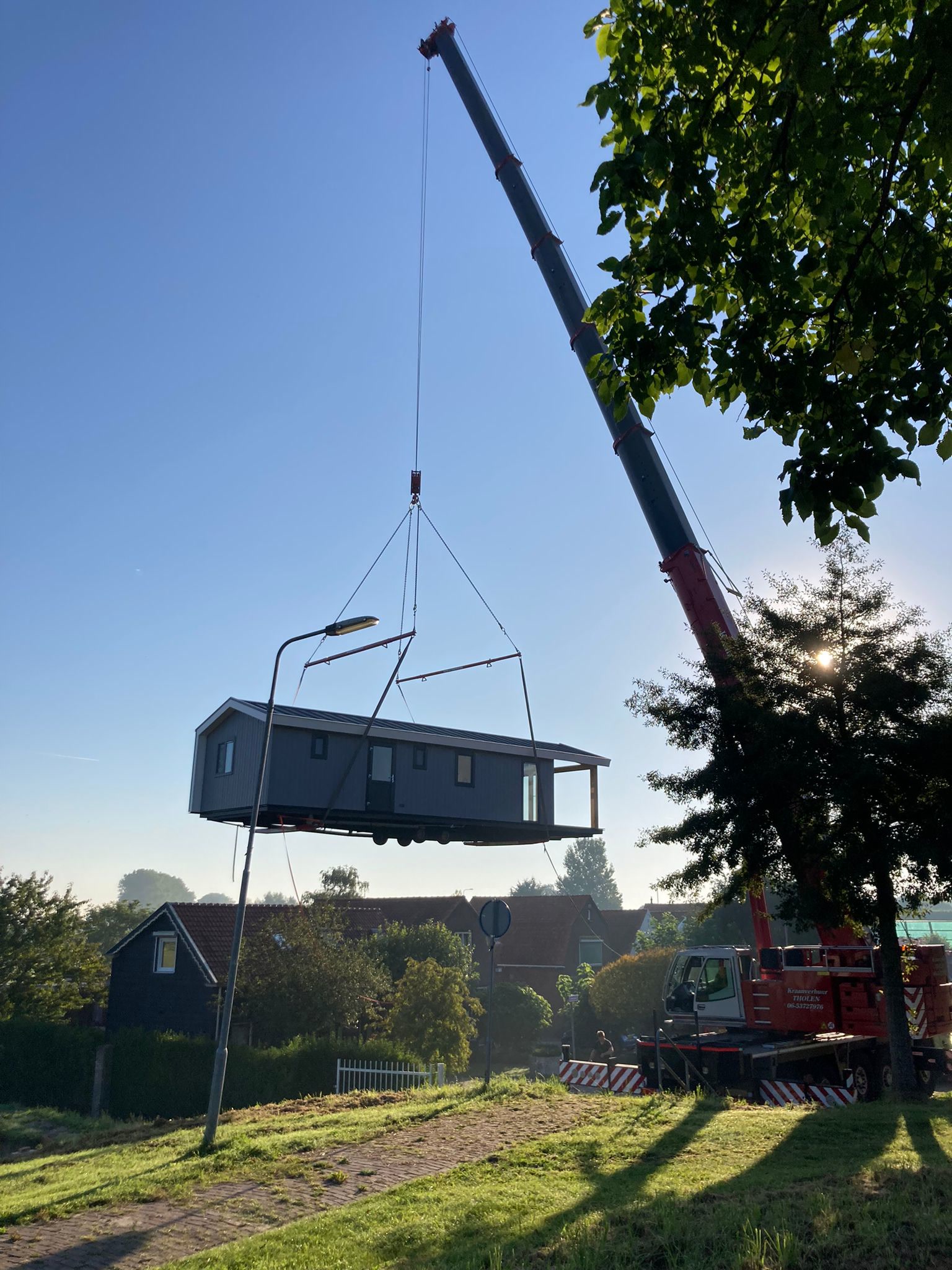 Een donkere woning hangt aan een kraan boven een dijk, in de ochtendzon